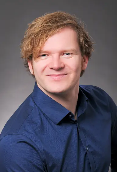 a blond male person facing the front camera with a dark blue shirt